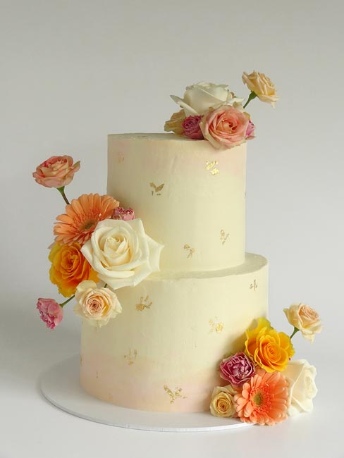 2-tier wedding cake with pink tinge, gold accents and warm-coloured flowers